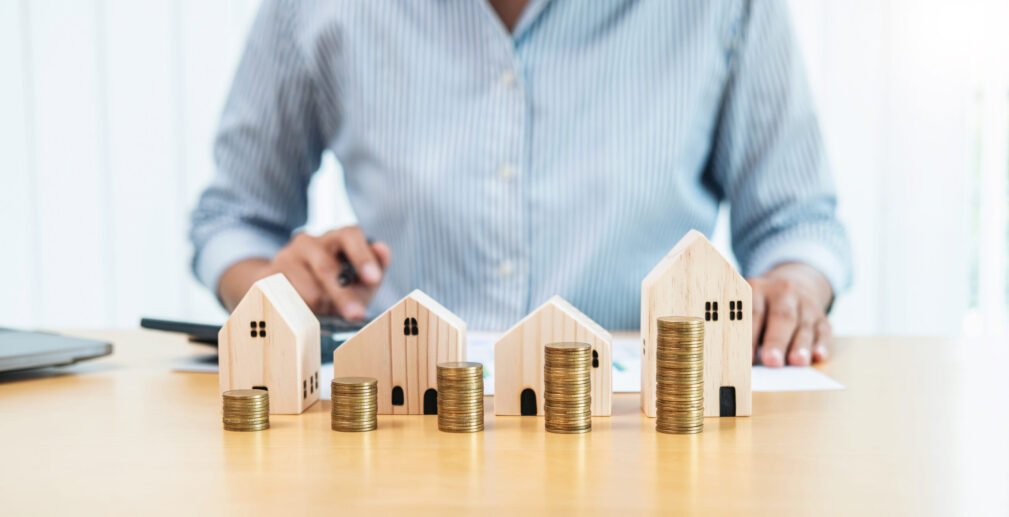 Asian business woman using calculator to calculate financial fro Asian business woman using calculator to calculate financial from chart document for buy house mortgage and property investment with having many house model and stack coins on the table