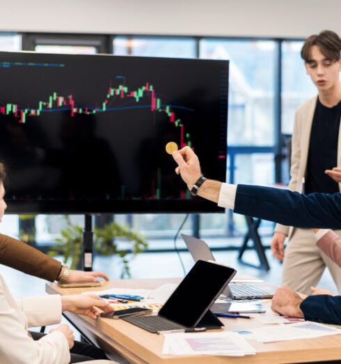 Young worker leading business meeting about cryptocurrencies in an office Young worker leading business meeting in an office, discussing the topic of cryptocurrencies with other workers using a big display with currency rate and physical coin