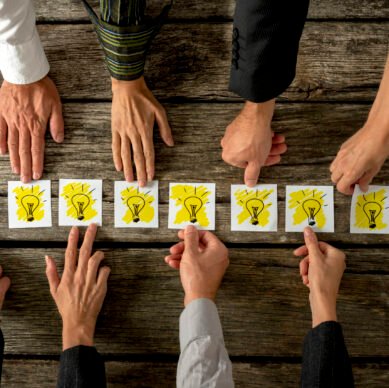 Brainstorming and teamwork concept with a group of diverse business people each holding out a card with a shining light bulb arranged in a row conceptual of ideas, inspiration and innovation.