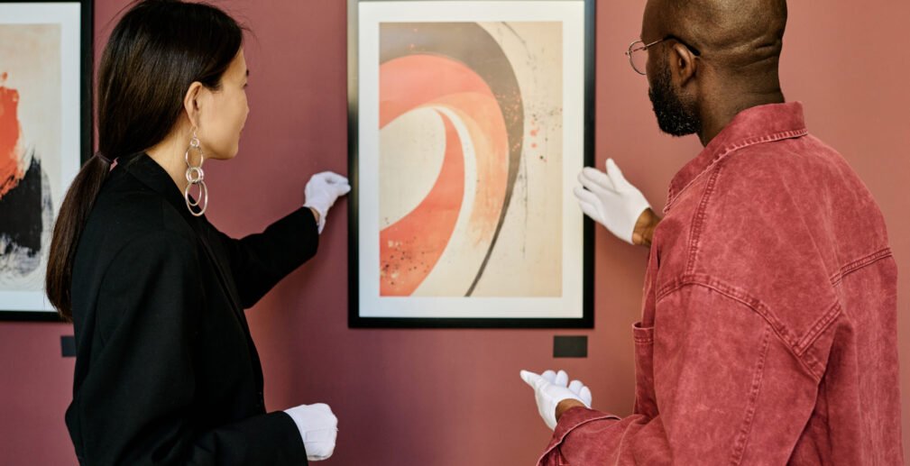 Observing and Discussing Art at Exhibition Gallery staff dressed in dark and casual attire, discussing modern abstract painting hanging on wall in gallery. Stylish ambiance underscores engagement with art