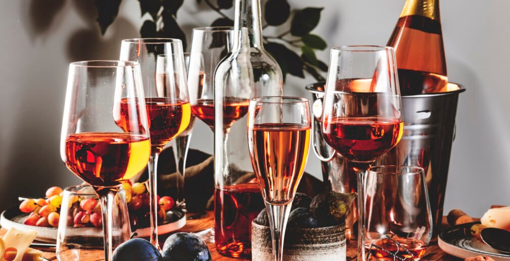 Pink rose wine glasses and bottles on table served for summer fe Pink rose wine glasses and bottles on table served for summer festive dinner party with different kinds of appetizers